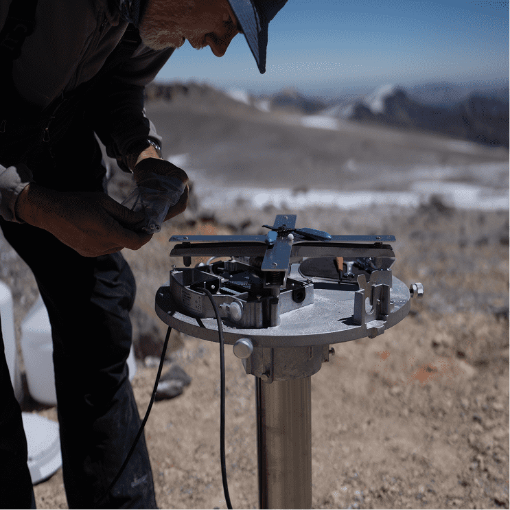 A man installing a sensor on top of a mountain