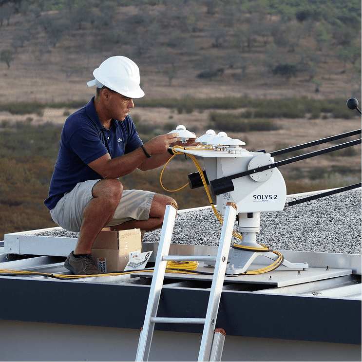 A man on a roof kneeling down inspecting a solys 2 sun tracker